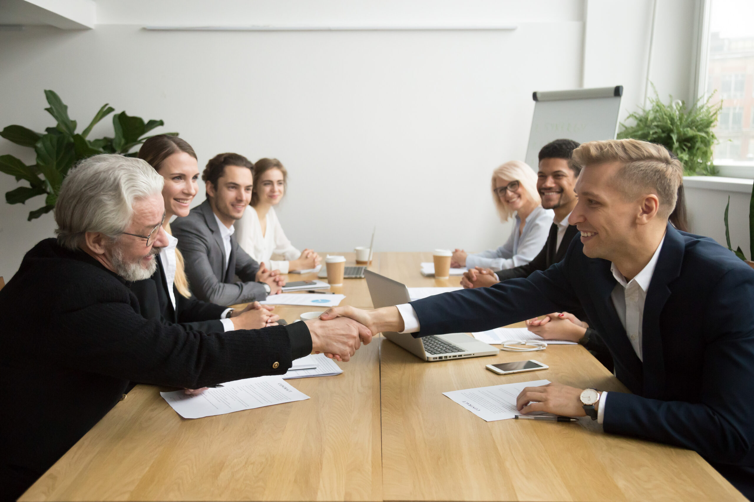 Senior investor buying startup handshaking young entrepreneur at